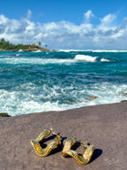 Gold proof of beauty hoop earrings on a rock with ocean and sky in the background